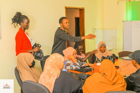Two facilitators stand and guide a discussion with young women seated around a meeting table.