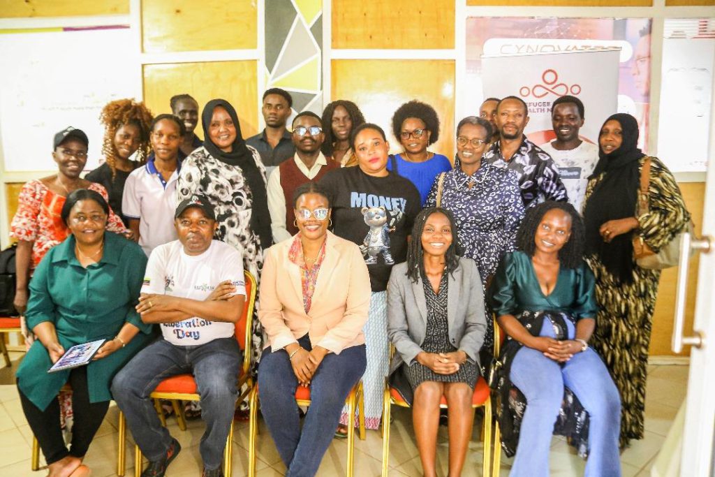 About twenty workshop participants pose together indoors, some seated and some standing, in front of an RMHN banner.
