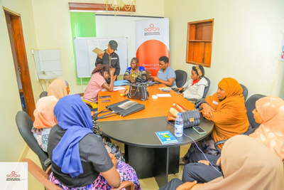 Women and young people sit around a round table during an RMHN session, notebooks open.